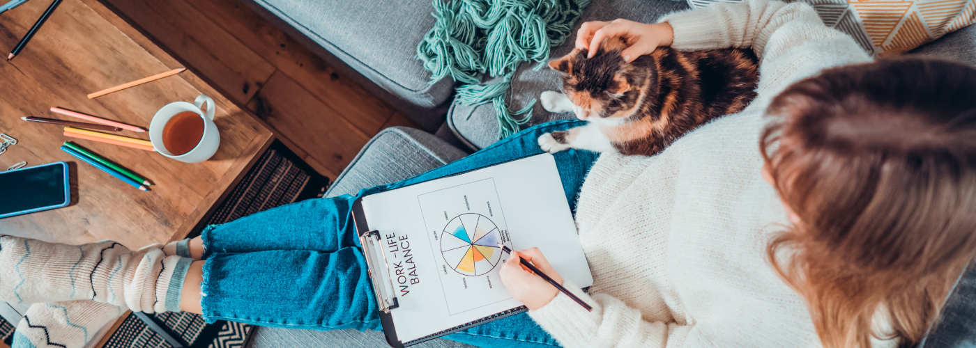 A woman on the coach with her cat with a piece of paper that says "work-life balance"