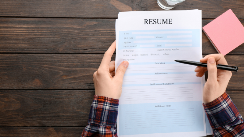 A person looking at a resume with a pen in hand waiting to fill it out.