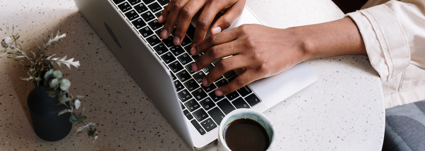 A person typing on a laptop with a cup of coffee nearby.