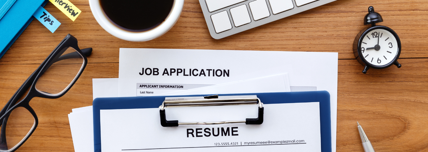 Papers on a desk relating to a job application and a top of a resume showing.