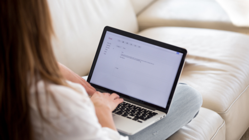 A woman sitting on a couch, engrossed in her laptop, focused on her work.