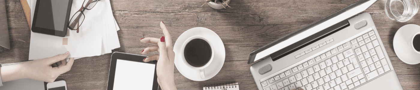 Bird-eye view of a table with people's hands working with coffee, papers, pens and other office supplies scattered