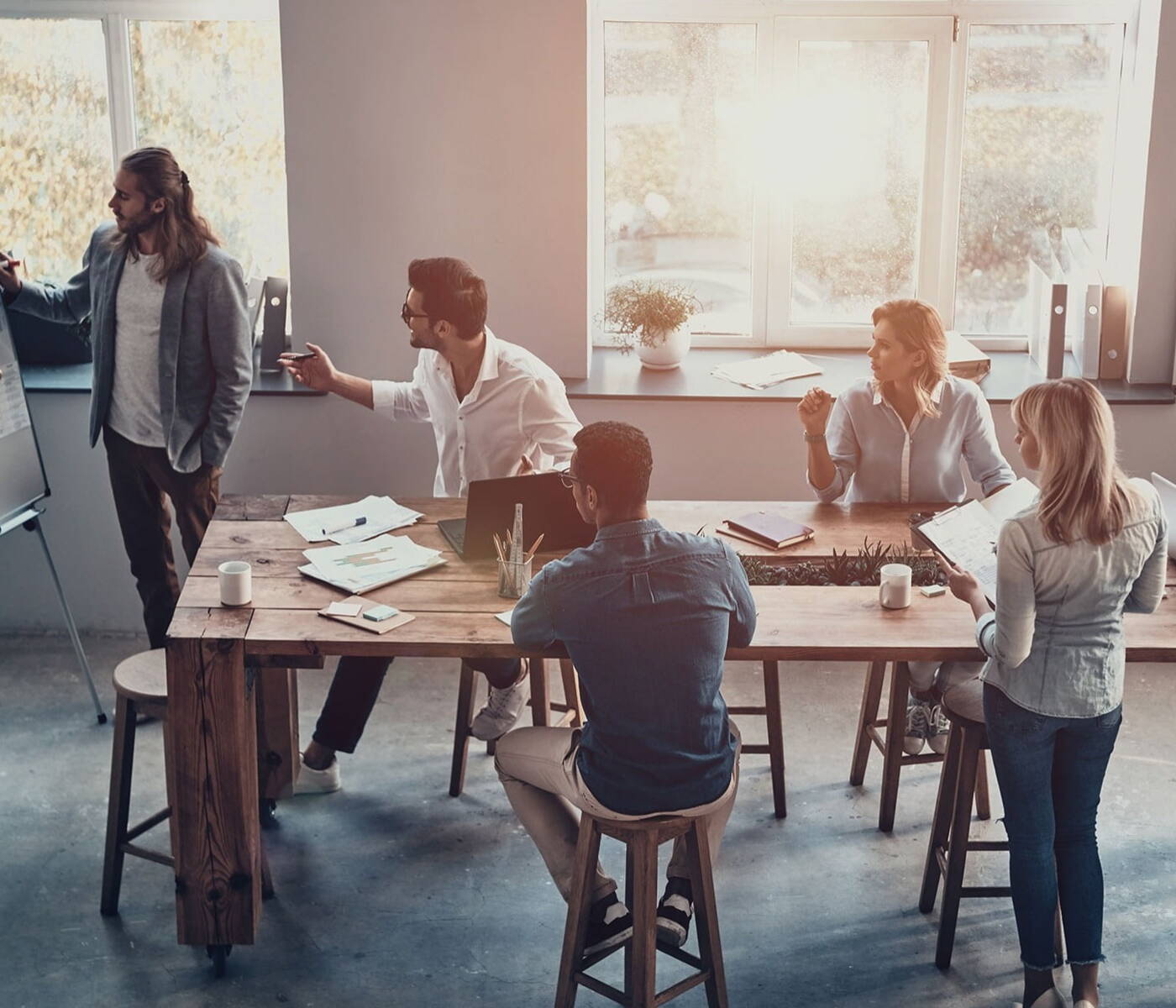 Businessman standing to present an idea to a group of professionals sitting around a meeting table 